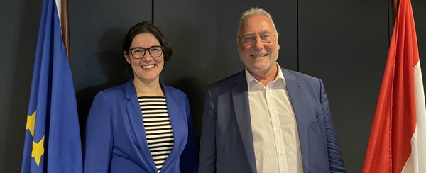 Martine Ouwersloot en Eduard Dame lachen in de camera, staand tussen de Europese vlag en de Nederlandse vlag