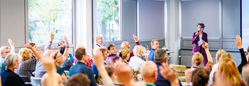 Overzicht van de zaal op de bijeenkomst 9 oktober. Een aantal deelnemers steekt de vingers omhoog